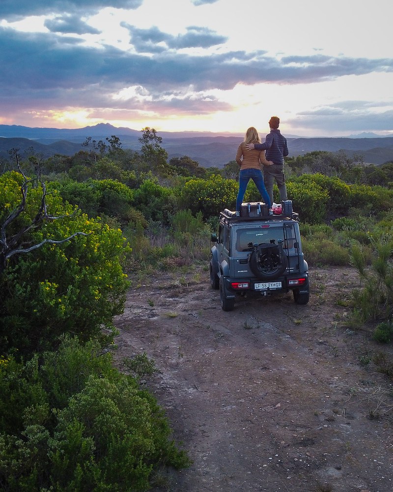 Couple standing on car roof enjoying the sunset